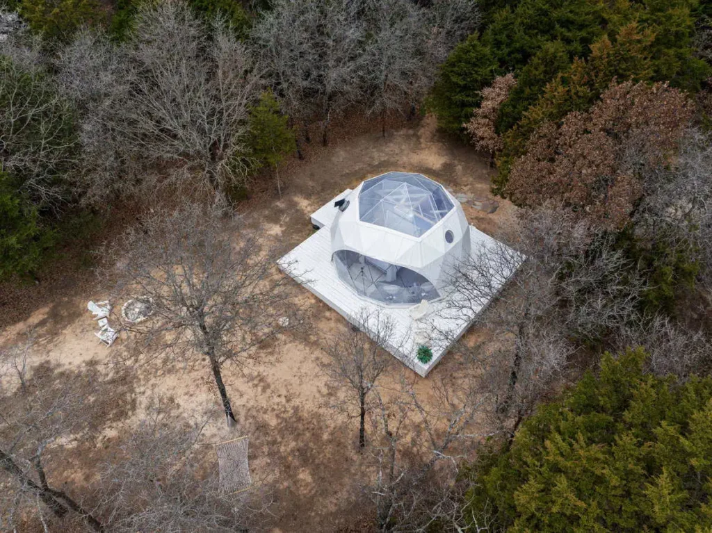 Aerial view of the Escape Velocity Dome, a unique geodesic lodging surrounded by trees, featuring a spacious deck and outdoor seating area.