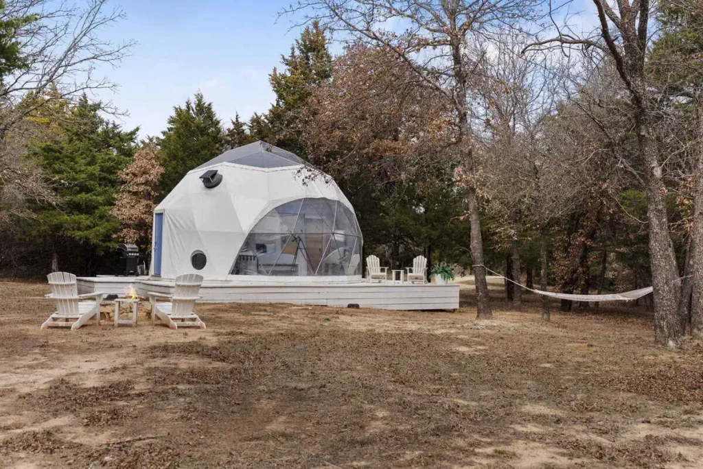 Escape Velocity dome accommodation surrounded by trees, featuring a fire pit and hammock, designed for unique lodging experiences.
