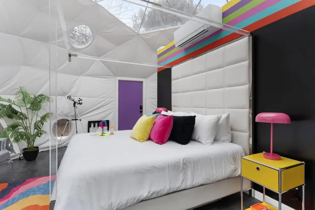 Colorful interior of the Mod Squad dome at All Is Well Resort, featuring a white bed with vibrant pillows, modern decor, and a cozy atmosphere.