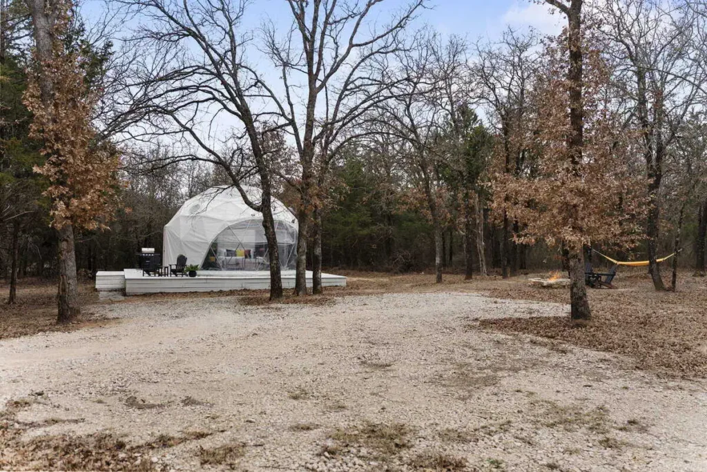 Dome accommodation at All Is Well Resort surrounded by trees, featuring outdoor seating, a fire pit, and a hammock for relaxation.