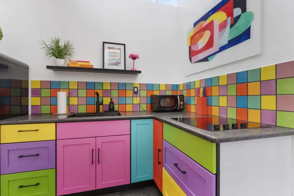 Colorful kitchen with vibrant cabinets in pink, green, and yellow, featuring a tiled backsplash and modern appliances, showcasing the unique design of the Mod Squad accommodation at All Is Well Resort.