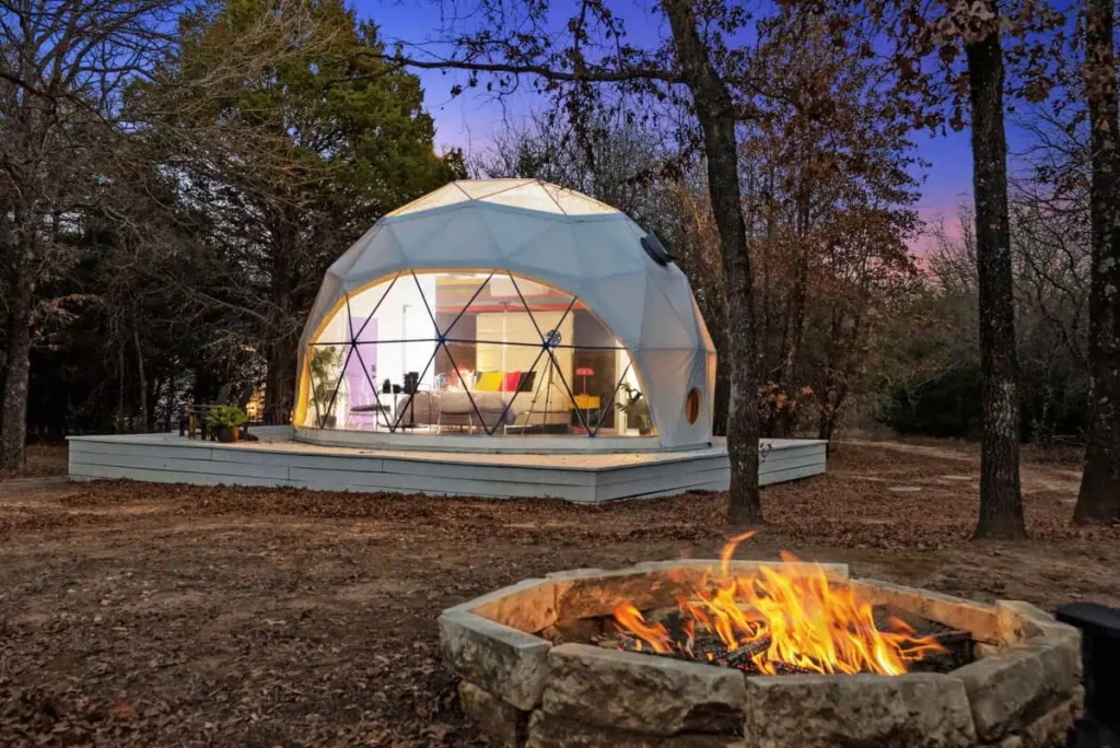 Dome accommodation at All Is Well Resort with outdoor fire pit, surrounded by trees at twilight.