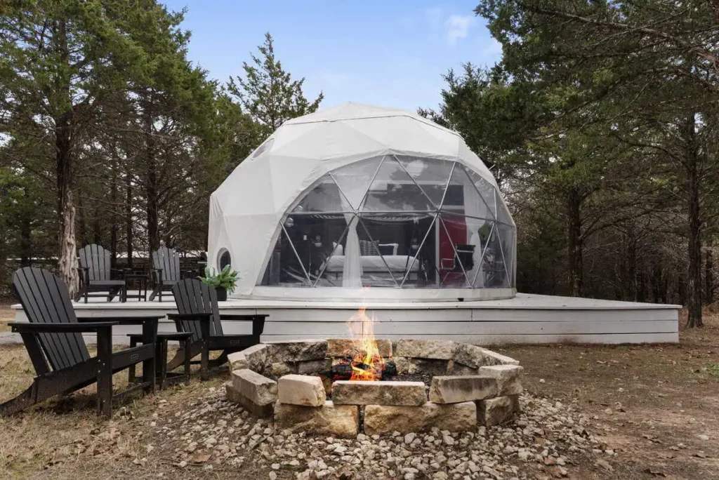 Geodesic dome accommodation at All Is Well St. Jo, featuring a fire pit and outdoor seating in a serene wooded setting.