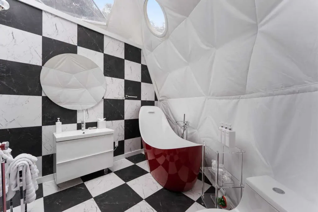 Stylish bathroom in Starman lodging featuring a modern red bathtub, sleek white vanity, and black-and-white checkered tiles, highlighting unique design and comfort amenities.