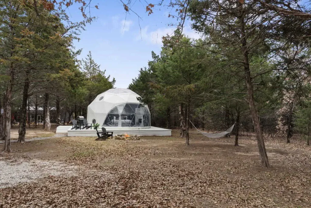 Dome-shaped accommodation at All Is Well St. Jo, surrounded by trees, featuring outdoor seating and a fire pit, emphasizing a serene and comfortable lodging experience.