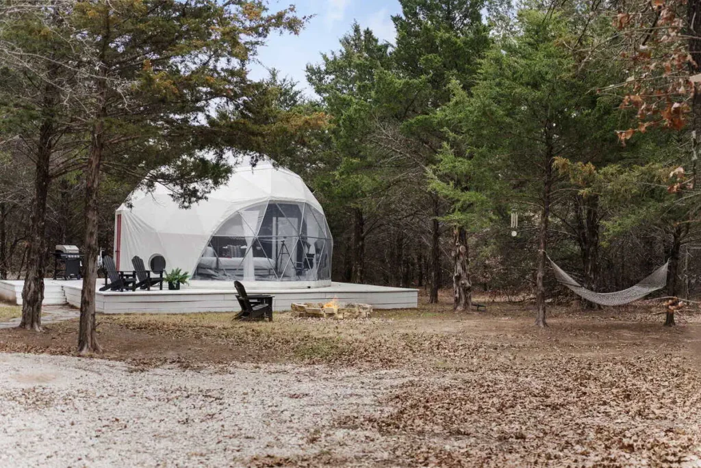 Dome-shaped accommodation at All Is Well St. Jo, featuring a hammock, fire pit, and outdoor seating surrounded by trees.