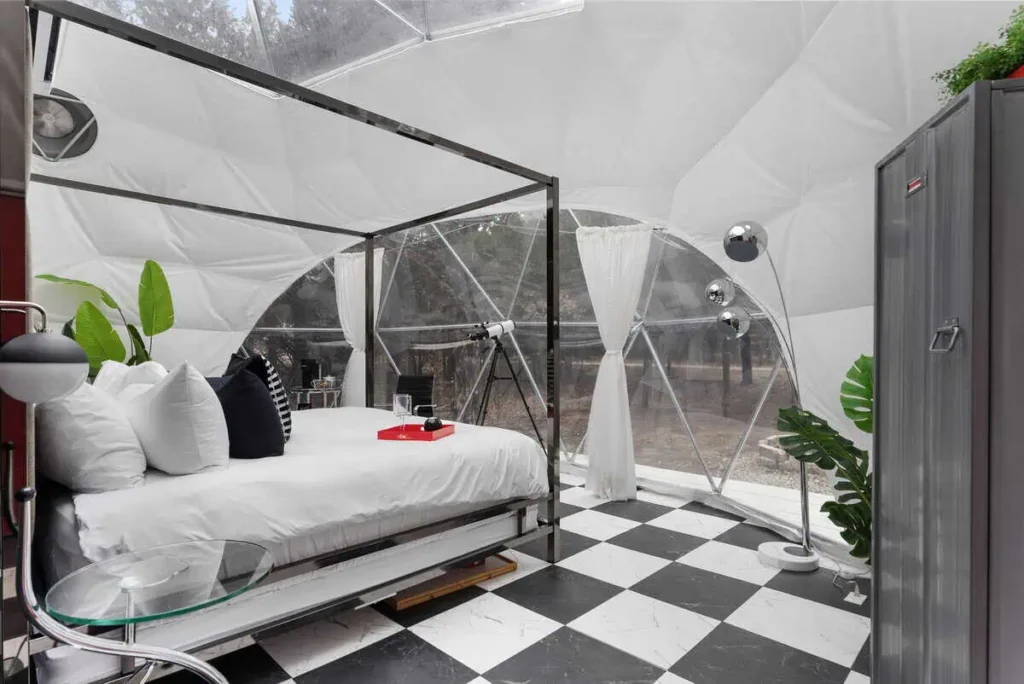 Interior of Starman lodging at All Is Well St. Jo, featuring a cozy bed with white linens, black and white checkered flooring, modern decor, and large windows for natural light.