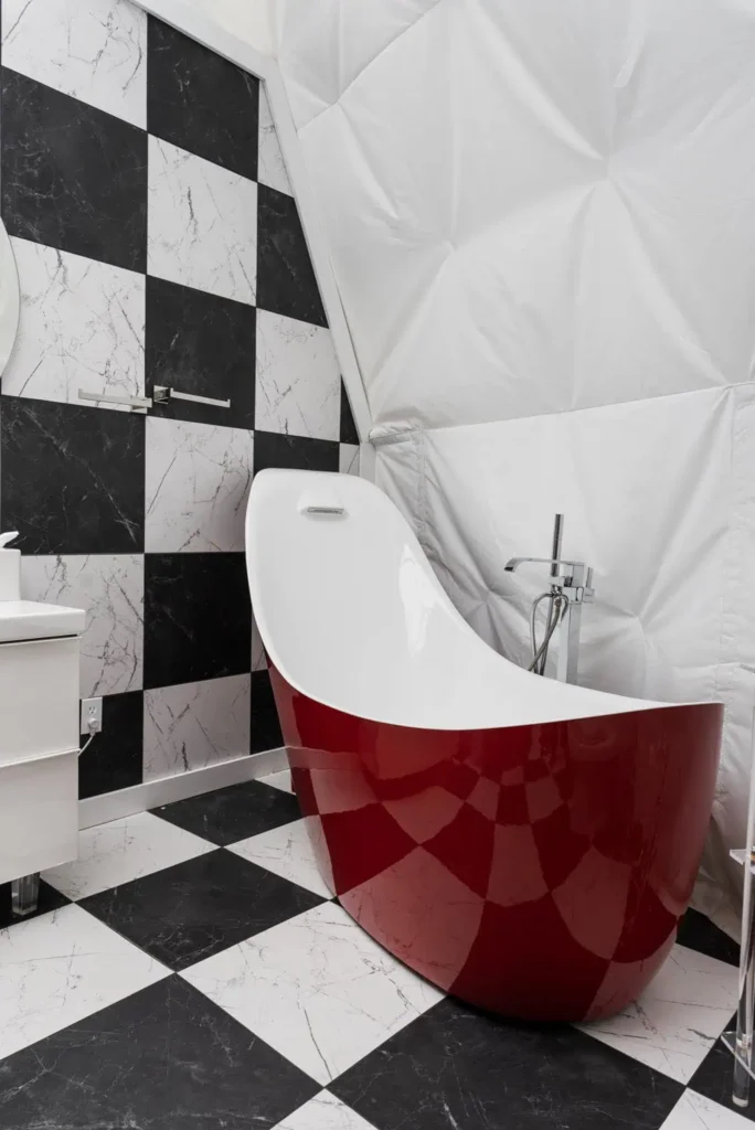 Modern bathroom featuring a sleek red freestanding bathtub, black and white checkered tile flooring, marble accent wall, and contemporary fixtures, highlighting luxurious amenities at Starman lodging, All Is Well St. Jo.
