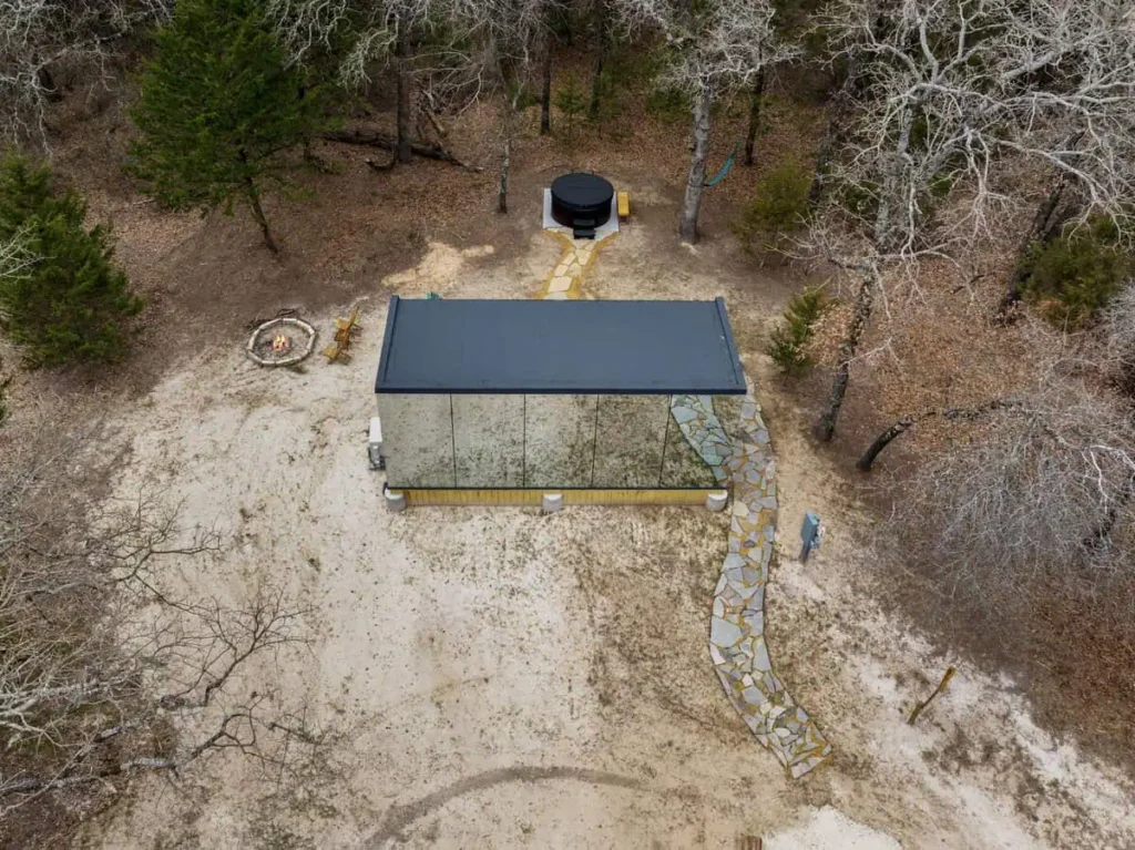 Aerial view of the Cosmic Cube accommodation featuring a modern design, surrounded by nature, with a pathway leading to a fire pit and hot tub, highlighting unique lodging experience at All Is Well.