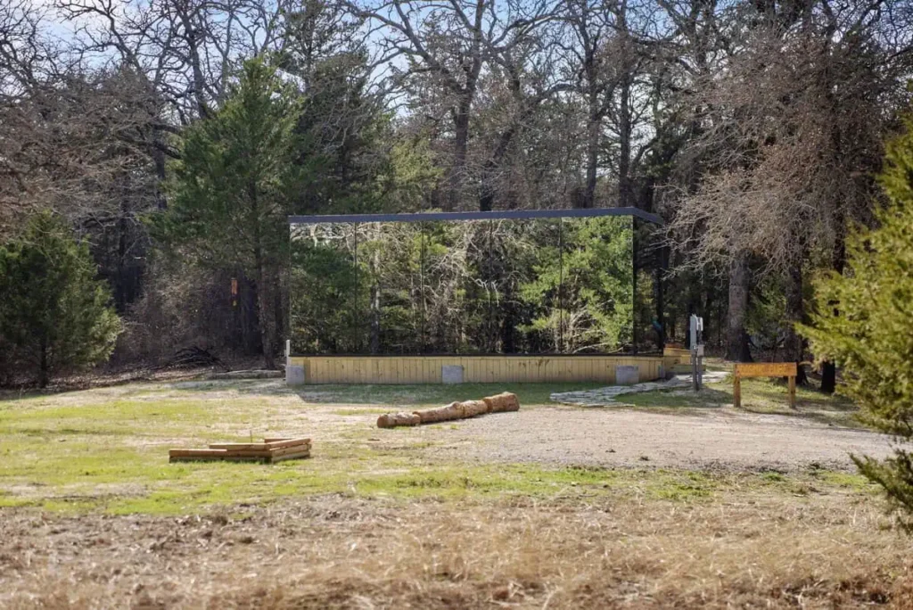 Mirror House exterior surrounded by trees, showcasing unique design of the Cosmic Cube accommodation by All Is Well, featuring natural surroundings and a serene setting for guests.