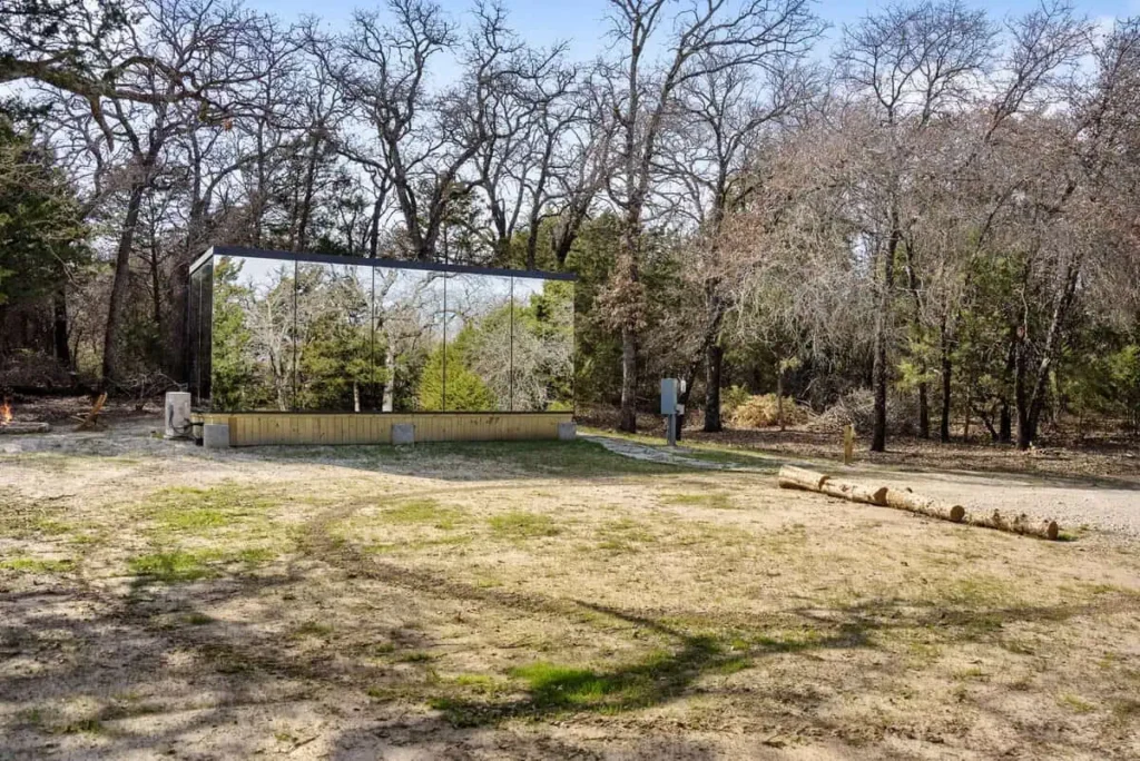 Mirror House of Cosmic Cube accommodation surrounded by trees, featuring reflective exterior, designed for unique lodging experience at All Is Well.