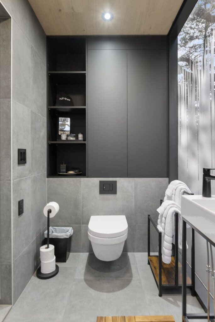 Modern bathroom interior featuring a wall-mounted toilet, sleek storage shelves, and minimalist decor, highlighting the tranquil ambiance of the Music Box accommodation at All Is Well Resort.