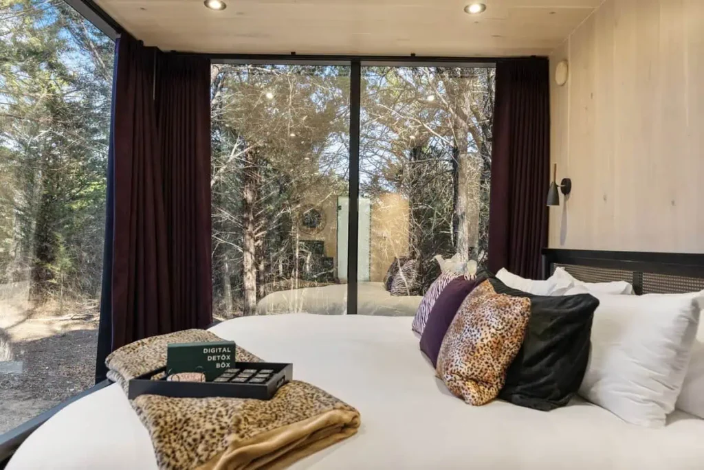 Cozy bedroom in Music Box yurt with large windows, plush bedding, and a digital detox box, surrounded by nature at All Is Well Resort.