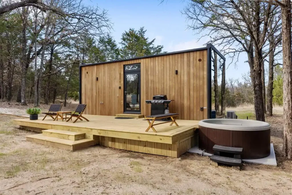 Music Box yurt accommodation at All Is Well Resort featuring a wooden deck, hot tub, outdoor seating, and grill, surrounded by trees in a tranquil natural setting.