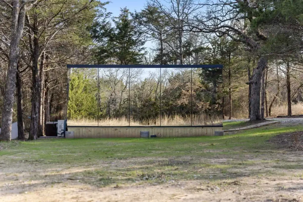 Mirror House exterior in natural setting, surrounded by trees, showcasing reflective glass walls, part of Music Box lodging at All Is Well Resort.