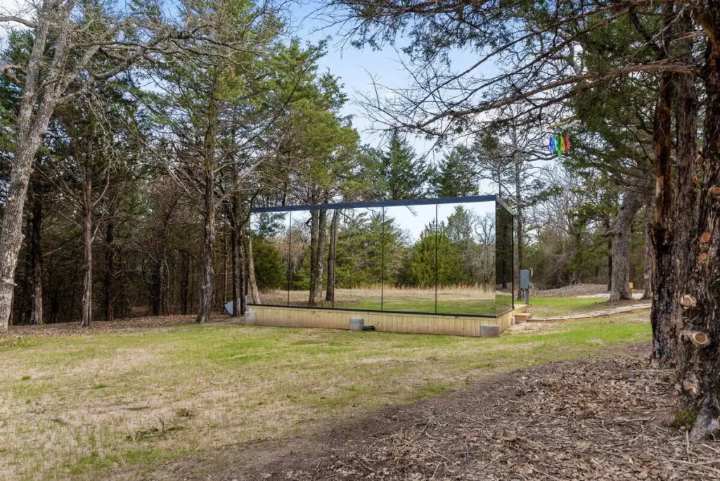 Mirror house surrounded by trees, reflecting nature, showcasing unique lodging at All Is Well Resort's Music Box accommodation.