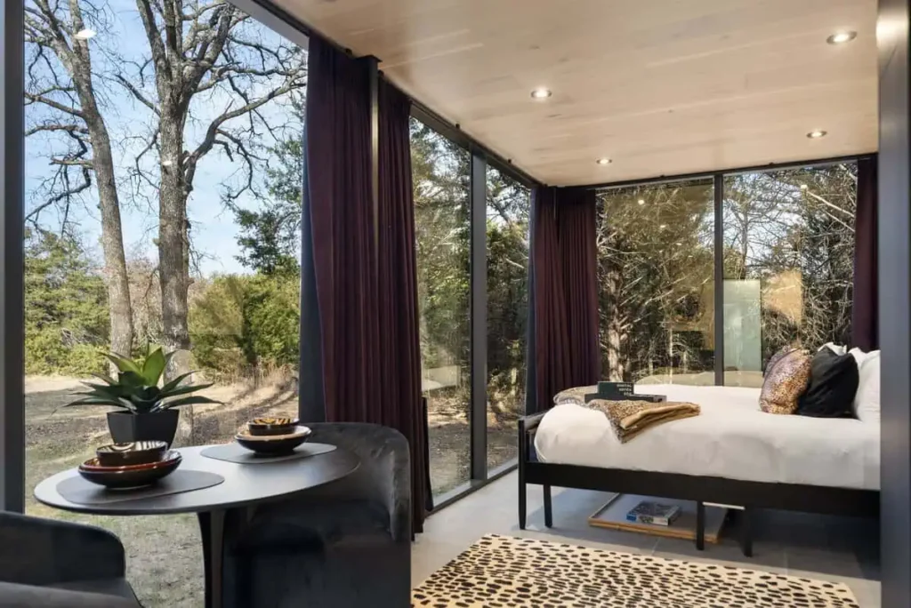 Modern interior of Music Box yurt at All Is Well Resort, featuring a cozy bed, dining table, and large windows with views of surrounding nature.
