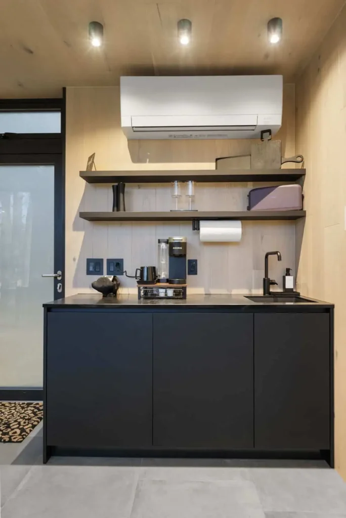 Modern kitchen area in Music Box yurt, featuring black cabinetry, microwave, mini fridge, Keurig coffee machine, air conditioning unit, and stylish decor.