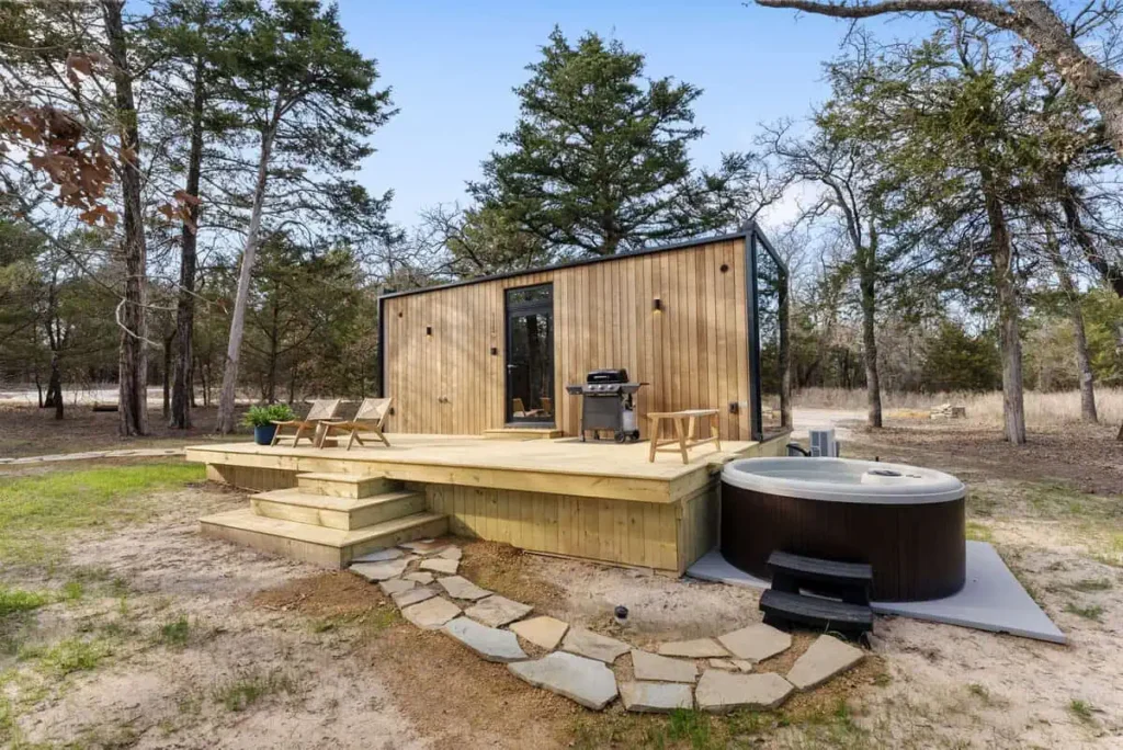 Zen Den accommodation with wooden deck, hot tub, and grill surrounded by trees, emphasizing relaxation and wellness amenities.