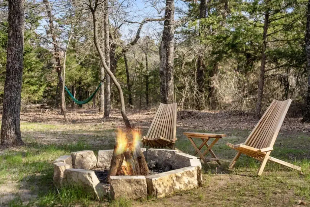 Fire pit surrounded by wooden chairs and a hammock in a tranquil wooded setting, highlighting outdoor relaxation at the Mirror House Yurt Retreat.