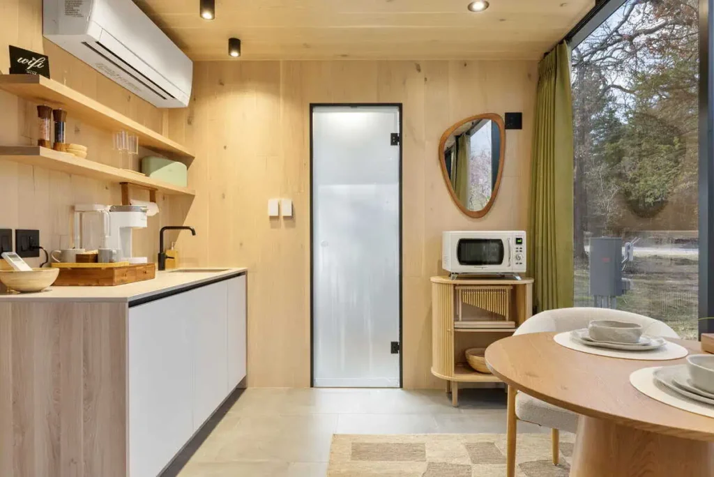 Modern kitchen interior of Zen Den accommodation featuring self check-in, microwave, mini fridge, Keurig coffee machine, and dining table, with natural light from large windows.