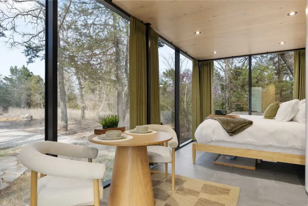 Interior view of the Zen Den at Mirror House, featuring a cozy bed, minimalist wooden table with dishes, large windows showcasing natural surroundings, and warm decor elements, emphasizing relaxation and tranquility.
