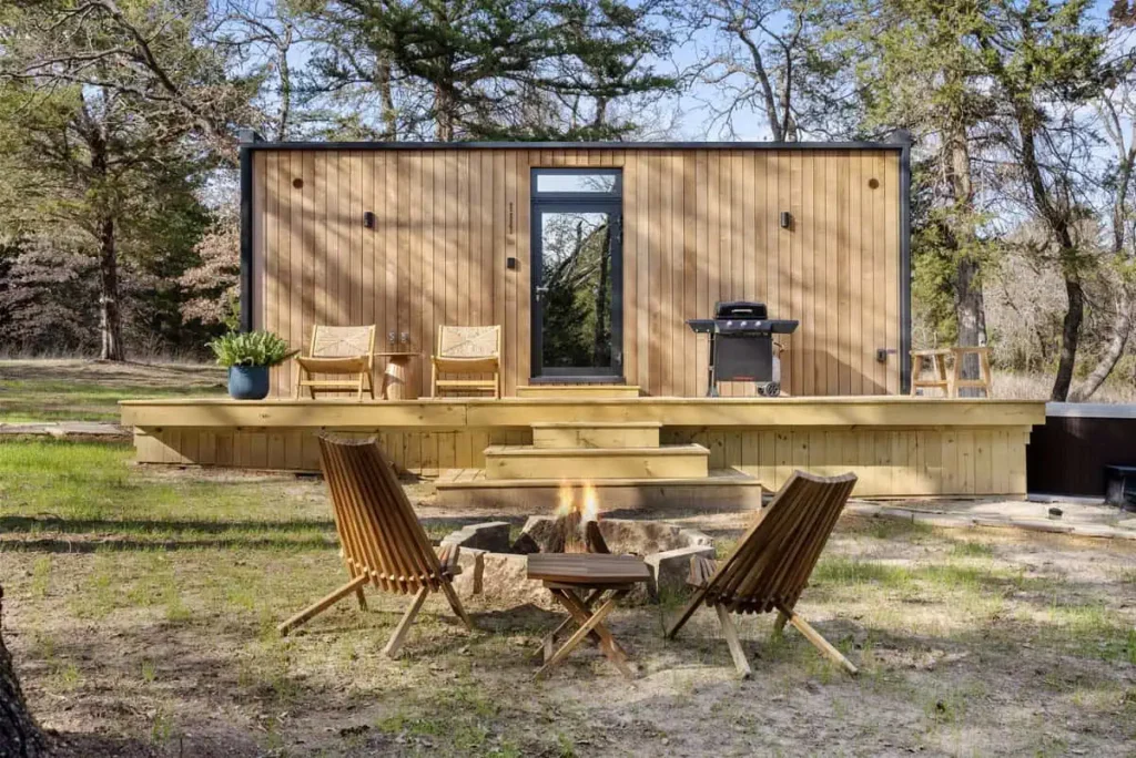 Mirror House yurt retreat with outdoor fire pit, wooden deck, and seating area, surrounded by trees, emphasizing relaxation and nature.