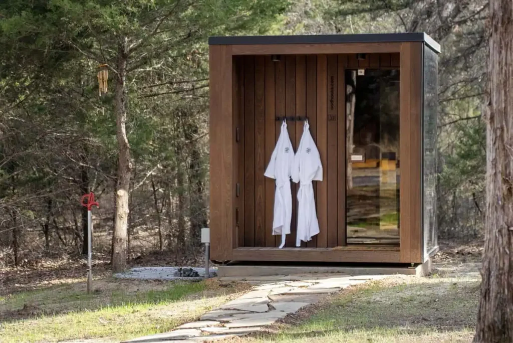 Sauna cabin in a natural setting, featuring hanging white robes, surrounded by trees, emphasizing relaxation and wellness at the Mirror House Yurt Retreat.