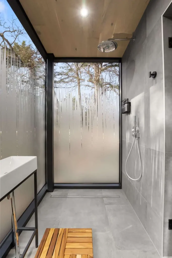 Modern shower space with wooden bench, frosted glass panels, and natural light, highlighting the Zen Den's relaxing atmosphere at All is Well St. Joe.