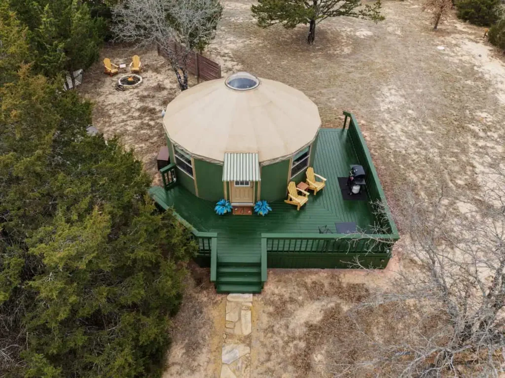 Aerial view of the 'Hippy Chick' yurt at All Is Well Resort, featuring a green deck, outdoor seating, fire pit, and natural surroundings, ideal for a unique glamping experience.