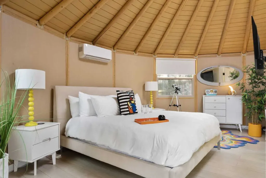 Cozy interior of the 'Hippy Chick' yurt at All Is Well Resort, featuring a queen bed, colorful decor, air conditioning, and natural light from windows, ideal for a serene getaway.