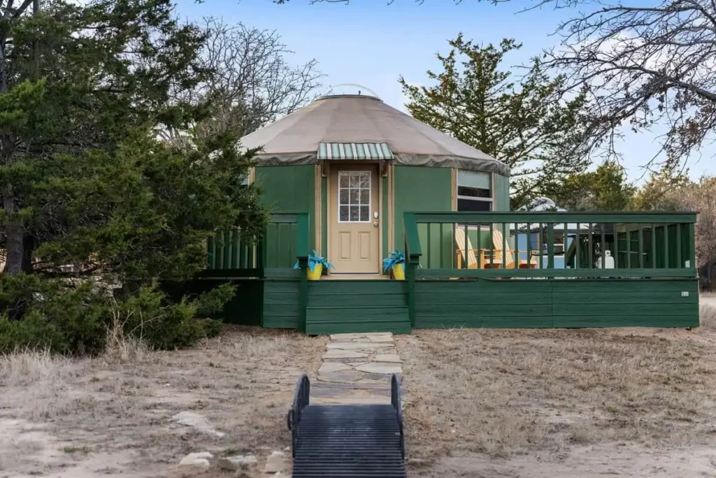 Hippy Chick yurt at All Is Well Resort, featuring green exterior, wooden deck, and surrounding natural landscape, ideal for glamping experiences.