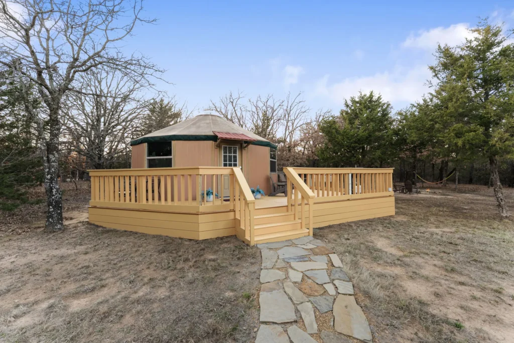 Glamping yurt with a large wooden deck and stone walkway in a forest clearing.