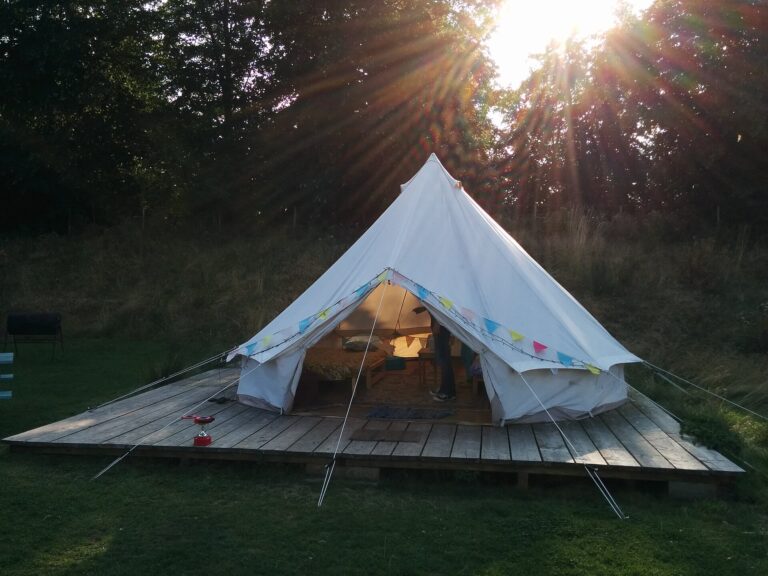 White canvas glamping tent on a wooden deck among trees with sunlight shining through