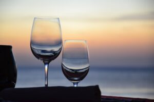 Two wine glasses silhouetted against a soft pink and orange sunset sky