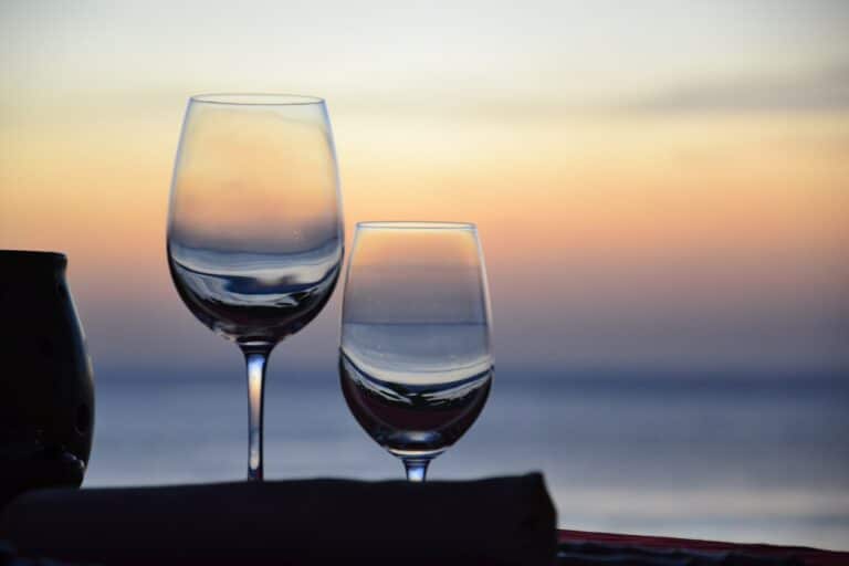 Two wine glasses silhouetted against a soft pink and orange sunset sky