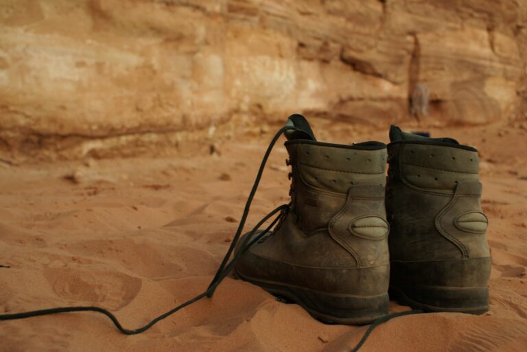 Pair of worn hiking boots with untied laces resting on sandy ground
