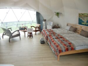 Bright interior of a glamping dome with a bed, lounge chairs and a curved geometric frame